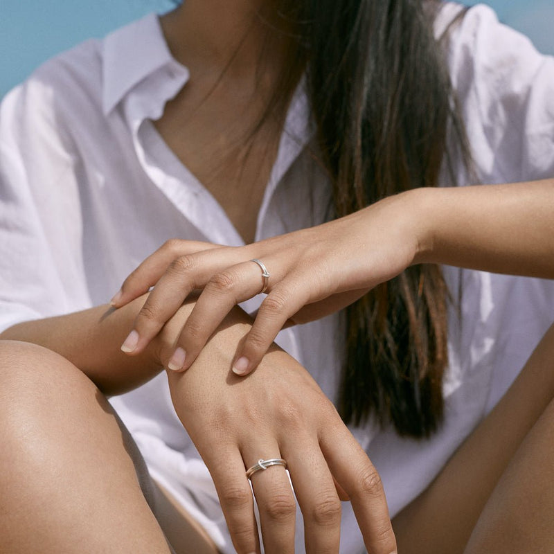Outdoor photo of a model sitting with a loose shirt. She has a ring on each hand,the Billie 1mm and  the Eden 2.1mm.