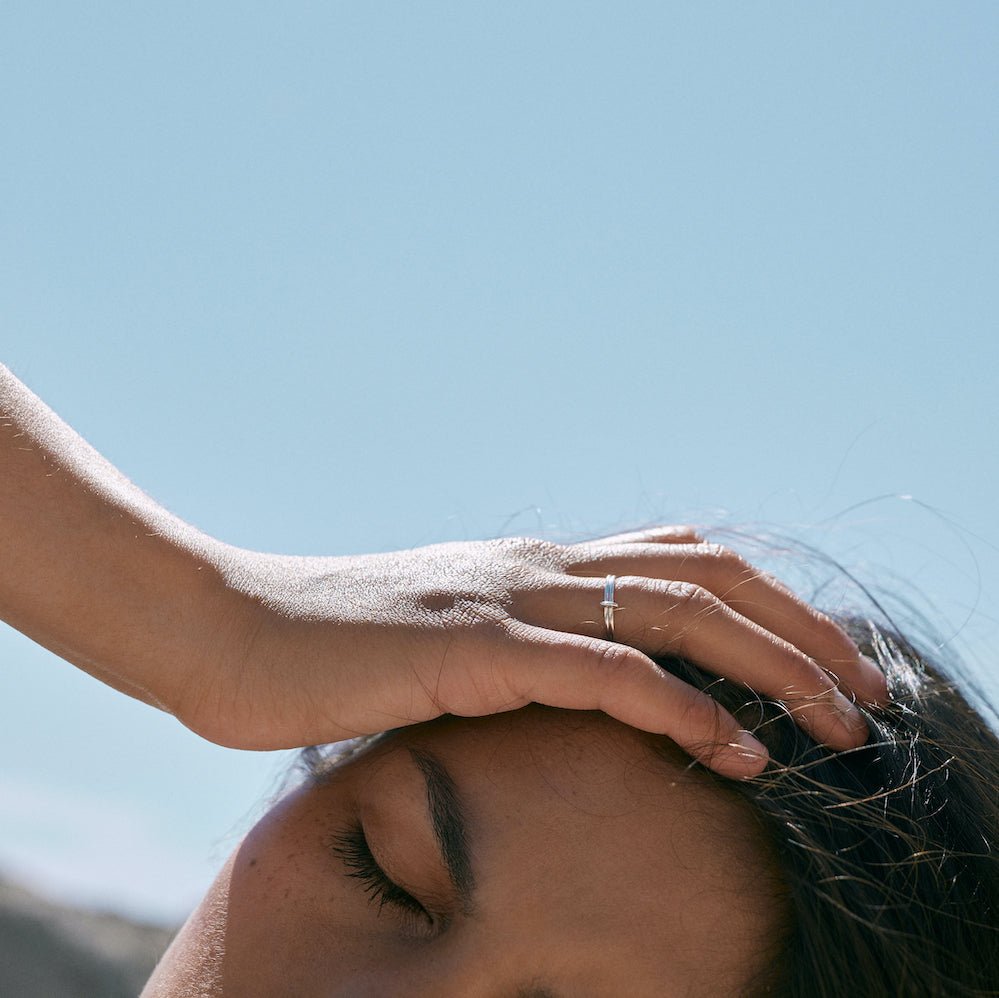Outdoor photo of a model wearing the Silver Billie 1mm ring. Her hand is placed on her head and she closes her eyes.