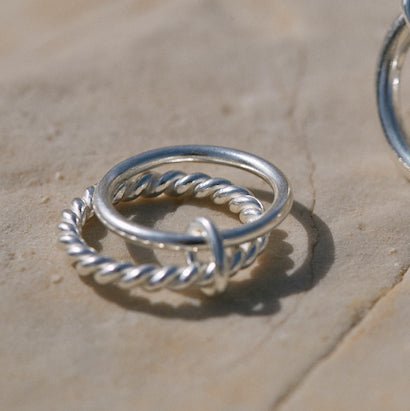 Photo on beige background of the Ellis ring in silver. It consists of 2 rings, one of 2mm diameter and the other is twisted.