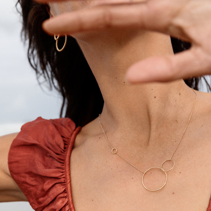 Outdoor photo of a model who is wearing the gold plated silver Trinity necklace. The model is wearing a red dress.